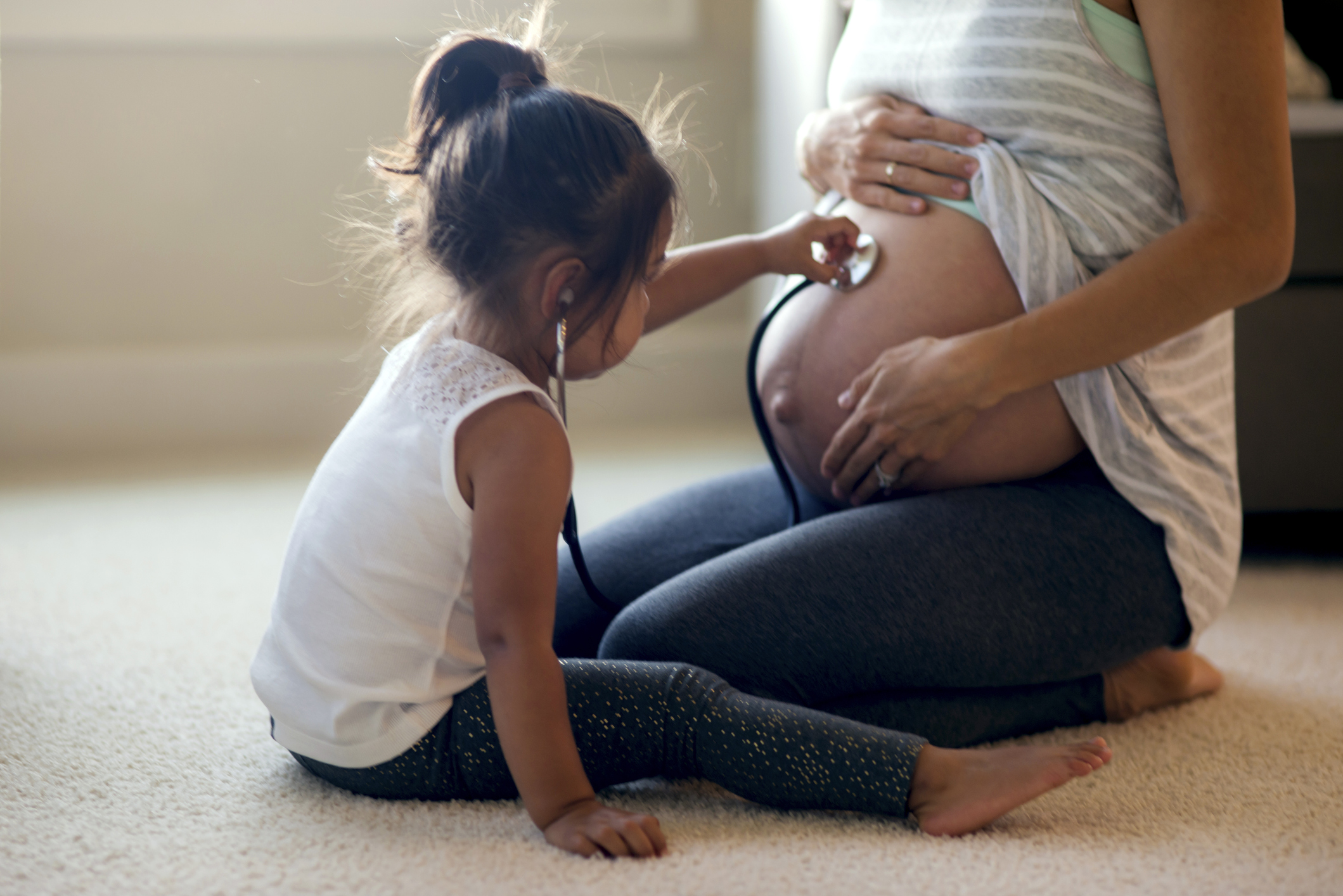 A young girl holds a stethoscope to a pregnant woman's belly
