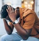 Shot of a stressed young afro-american man sitting on bench at the street and holding head with hands. Portrait of black man having a headache while sitting outdoor.